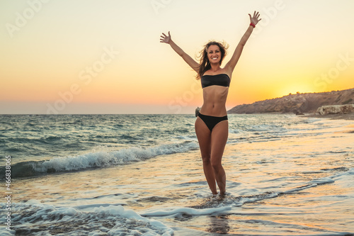 Young woman in bikini with raised hands and feel freedom at the beach
