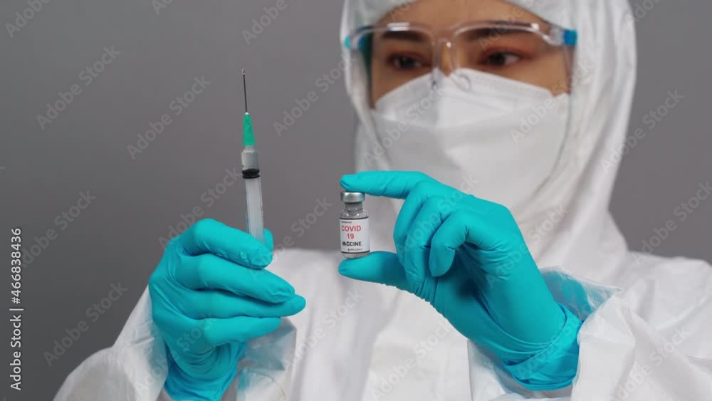 doctor in protective PPE suit holding Coronavirus (Covid-19) vaccine bottle and syringe injection medicine doctor in protective PPE suit holding Coronavirus (Covid-19) vaccine bottle and syringe injection medicine
