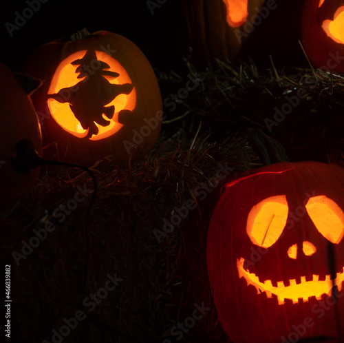 carved Halloween pumpkins in shapes of a witch flying on a broom stick the other a scary face both lit by candle light on a dark night representing all Hallows eve pumpkins glowing horizontal format  photo