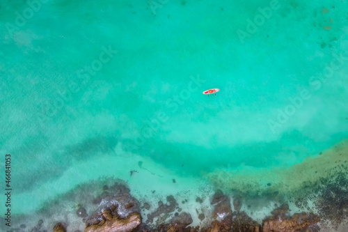 Aerial view of sea with coastal rocks, taken image from drone. Tourists are playing with surfboard in the sea.
