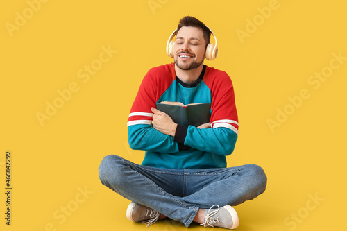 Happy man with headphones and book on color background © Pixel-Shot