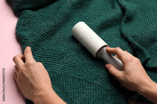 Woman cleaning green sweater with lint roller, closeup photo