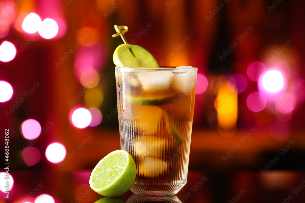 Glass of tasty Cuba Libre cocktail on table against blurred lights Glass of tasty Cuba Libre cocktail on table against blurred lights