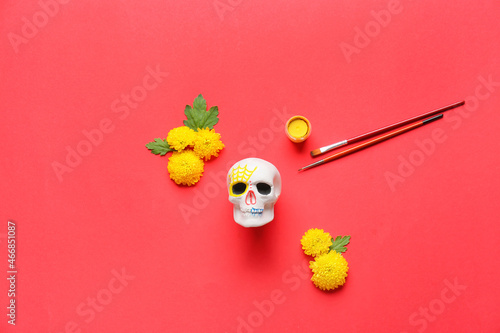 Painted human skull for Mexico's Day of the Dead (El Dia de Muertos) with brushes and flowers on red background