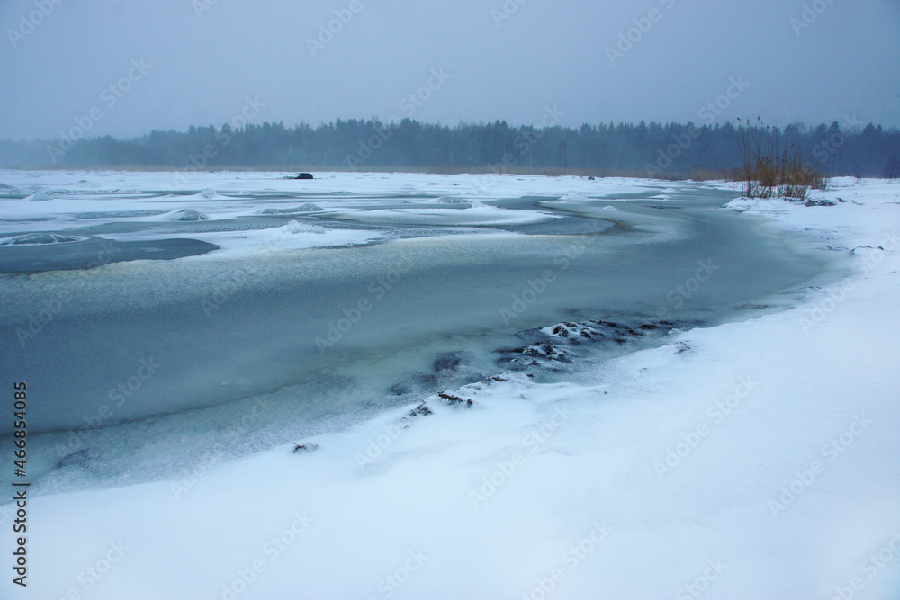 Winter landscape on the shore of a bay covered with snow and ice, snowing and poor visibility