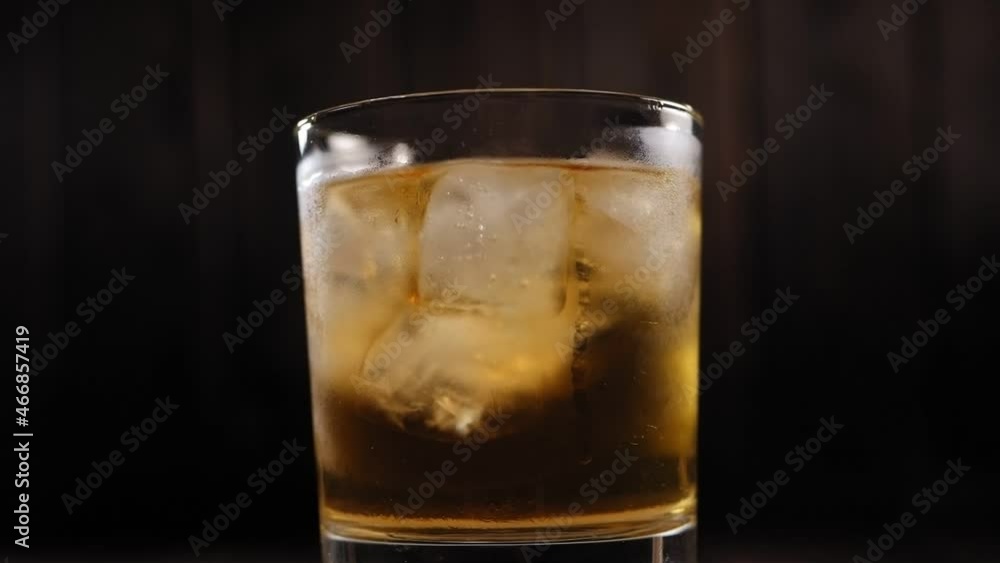 Close-up of a full glass of whiskey with ice slowly rotates on a black background. Slow motion. Image of a chilled alcoholic drink with ice. Close-up of a full glass of whiskey with ice slowly rotates on a black background. Slow motion. Image of a chilled alcoholic drink with ice.