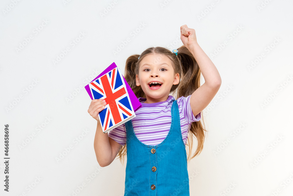 The schoolgirl happily jumps and holds an English textbook in her hands. The schoolgirl happily jumps and holds an English textbook in her hands.