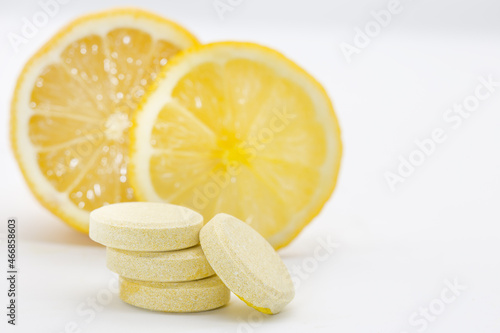 Vitamin  C  tablets on a white background. Cut lemons in the background.