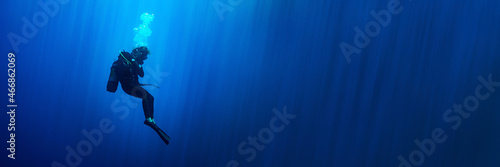 Background banner with a scuba diver woman standing still in deep blue with sun rays
