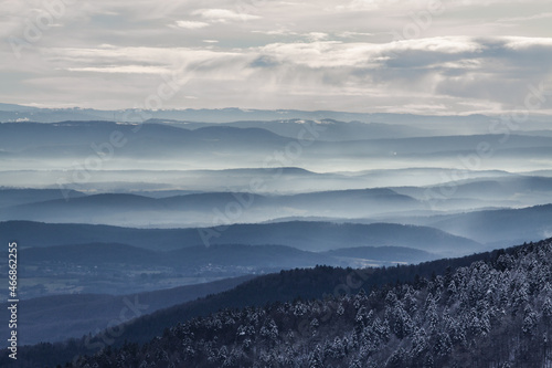 Wide panoramic view of mist landscape from the Vosges mountain range in France during winter covered with snow with dark mountains