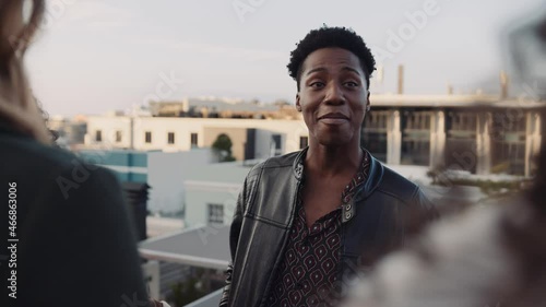 Black male socialising with a diverse group of adult friends at rooftop party. Chatting lightheartedly at dusk. High quality image. photo