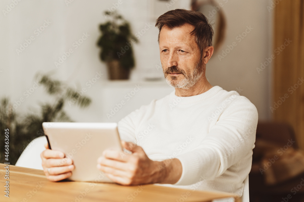 Senior man sitting reading on a tablet-pc at the dining table Senior man sitting reading on a tablet-pc at the dining table