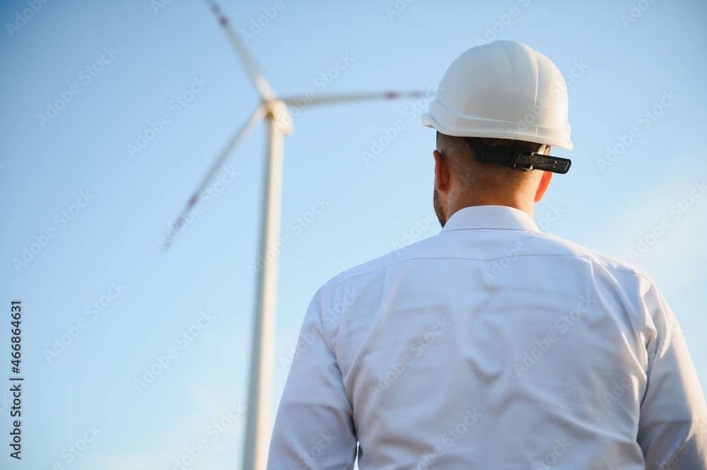 Engineer is checking energy production on wind turbine. Worker in windmills park in helmet. Engineer is checking energy production on wind turbine. Worker in windmills park in helmet.