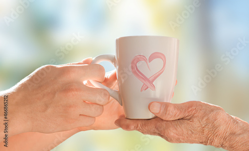 The hands of a young man serve a cup to the hands of an elderly woman. Care concept.