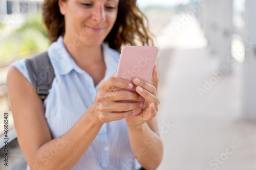 Horizontal view of unrecognizable woman in train platform with smartphone. Caucasian woman using technology and traveling in public transport. Travel and technology concept.