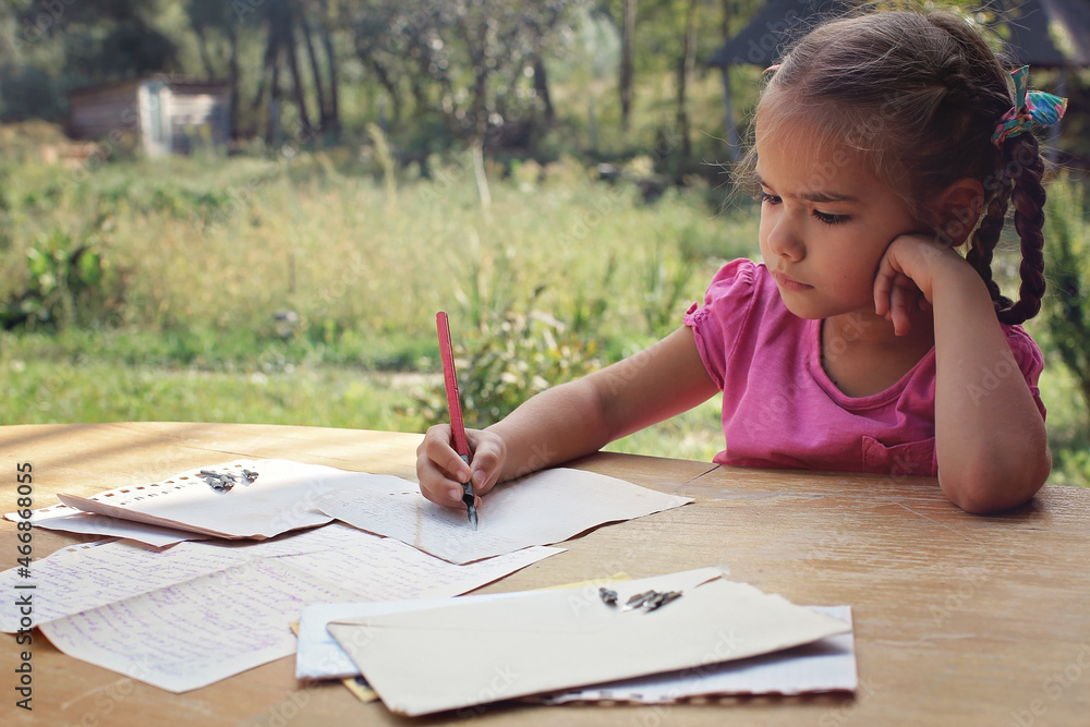 A little girl writing a letter with ink pen, old envelopes, ink pen and set of replacement pens on the aged wooden table, retro and vintage concept A little girl writing a letter with ink pen, old envelopes, ink pen and set of replacement pens on the aged wooden table, retro and vintage concept