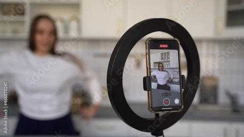 European girl records trendy dance moves in the kitchen on her smartphone camera. A young attractive girl dances for the social network tiktok.