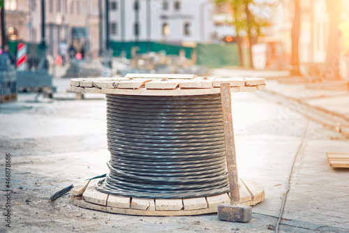 Spool with cable, wire spool - electric city communications, electricity supplying. Wooden coil with electric cable and optical fibers standing on the street, city street reconstruction. photo