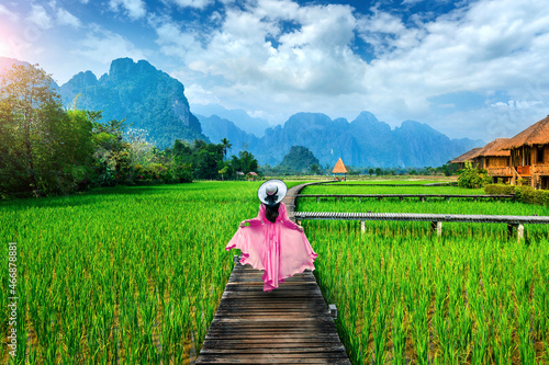 Young woman walking on wooden path with green rice field in Vang Vieng, Laos.