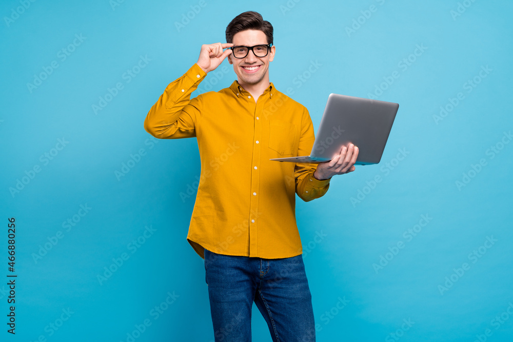 Photo of cheerful guy hold netbook shiny smile wear eyeglasses yellow shirt isolated blue color background Photo of cheerful guy hold netbook shiny smile wear eyeglasses yellow shirt isolated blue color background
