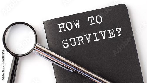 HOW TO SURVIVE business concept, magnifier with white text message on black notebook