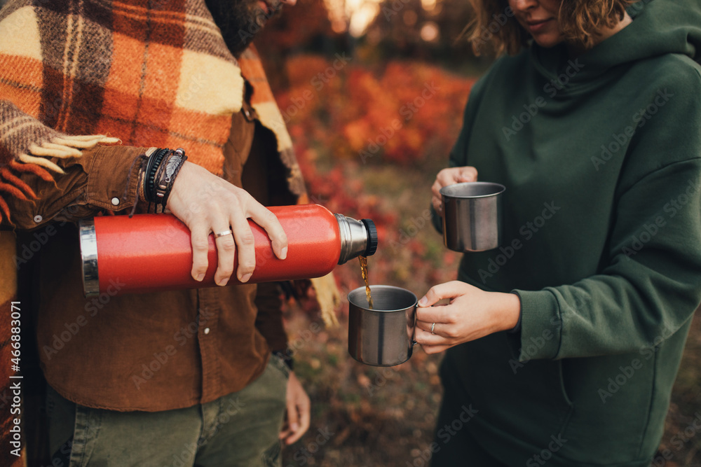 Naklejka premium Happy couple in love drinking tea from thermos in beautiful autumn forest.