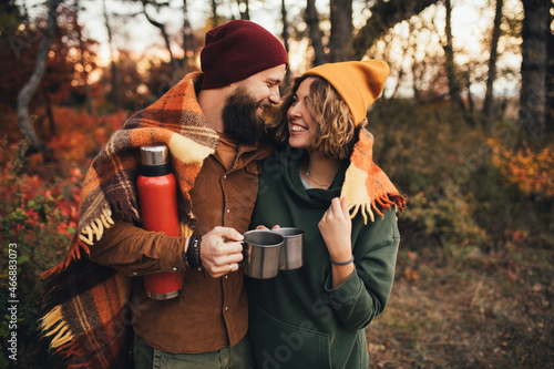 Happy couple in love drinking tea from thermos in beautiful autumn forest.