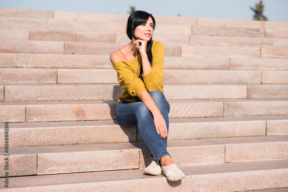 Beautiful and attractive caucasian brunette girl in a yellow sweater posing while sitting on the steps. Beautiful and attractive caucasian brunette girl in a yellow sweater posing while sitting on the steps.
