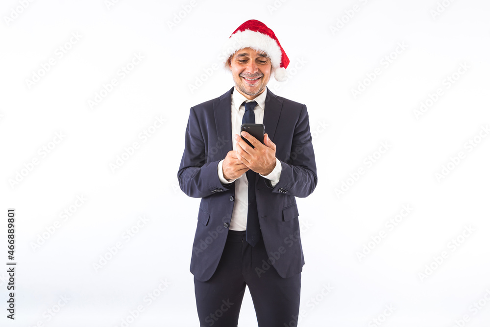 Businessman dressed in suit, tie and Christmas hat of Santa Claus, looking at mobile phone, on white background. Christmas celebration concept. Businessman dressed in suit, tie and Christmas hat of Santa Claus, looking at mobile phone, on white background. Christmas celebration concept.