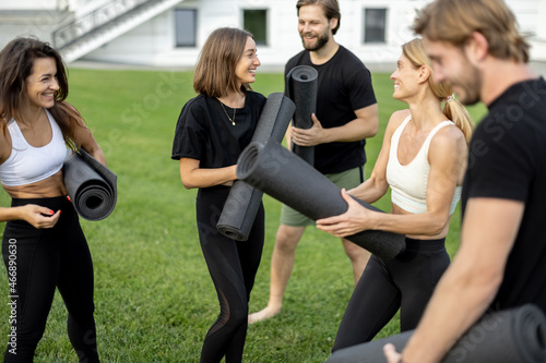Group of european people walking with fitness mats on green meadow. Friends practicing yoga and sport exercises. Concept of healthy lifestyle. Athletic men and women barefoot and wear sportswear
