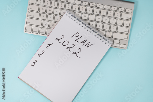 Business concept of 2022 goals list with notebook and keyboard on a blue background, top view