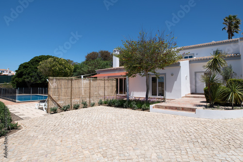 Front driveway of white portuguese villa with trees and calcada tiles