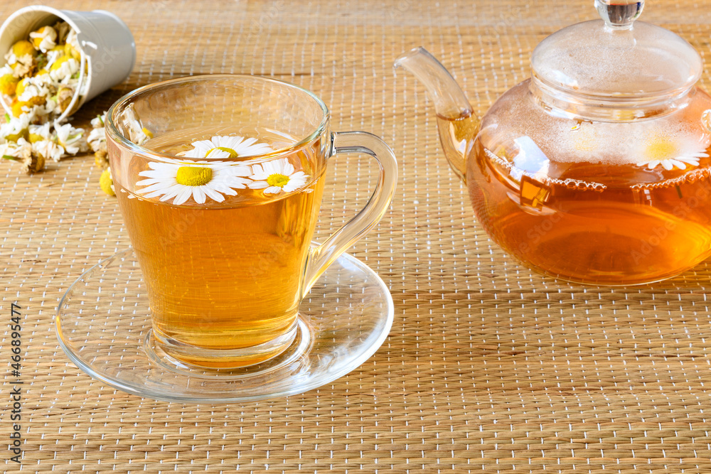 Healthy herbal tea with chamomile flowers in cup and teapot on rattan matting Healthy herbal tea with chamomile flowers in cup and teapot on rattan matting