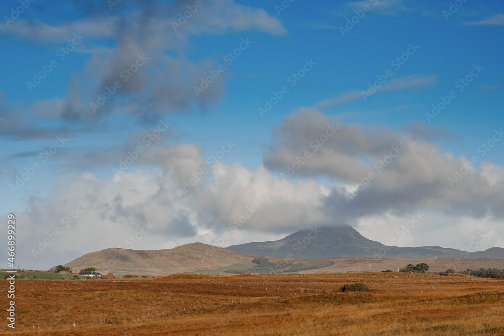 Vast empty field and Croagh Patrick mountains with clouds look like volcano eruption. Stunning Irish landscape. Beautiful nature scene with blue cloudy sky. County Mayo, Ireland