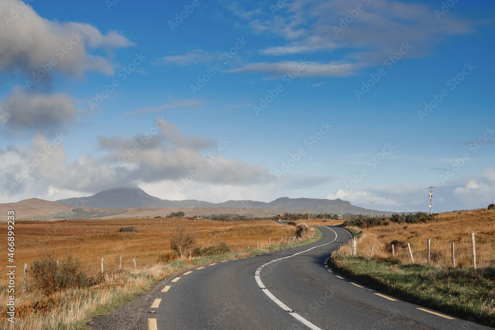 Small S shape asphalt road in a country side. Croagh Patrick mountain on the left in clouds. Travel in Ireland. county Mayo. Stunning Irish landscape. Blue cloudy sky. Road trip concept