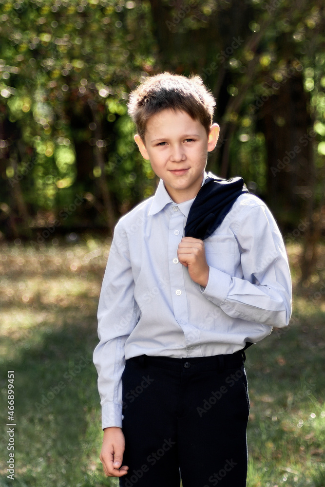 Portrait of a schoolboy looking into the camera on a blurry background of green trees. Portrait of a schoolboy looking into the camera on a blurry background of green trees.