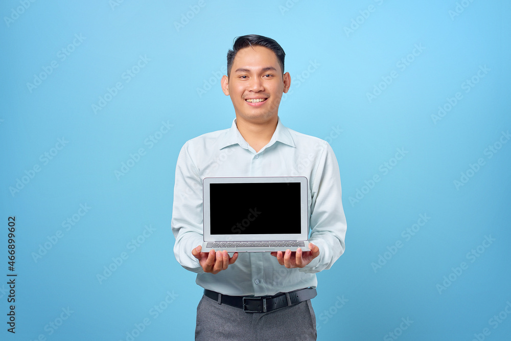 Smiling young handsome businessman showing a laptop with blank screen on blue background Smiling young handsome businessman showing a laptop with blank screen on blue background