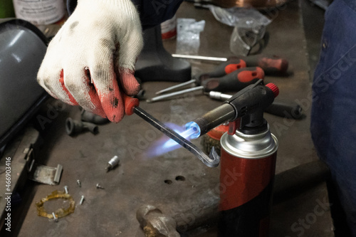 A crafstman holding a small blowtorch and working on a metal design project by burning the metal and making it look old, dark and rusty, brown color