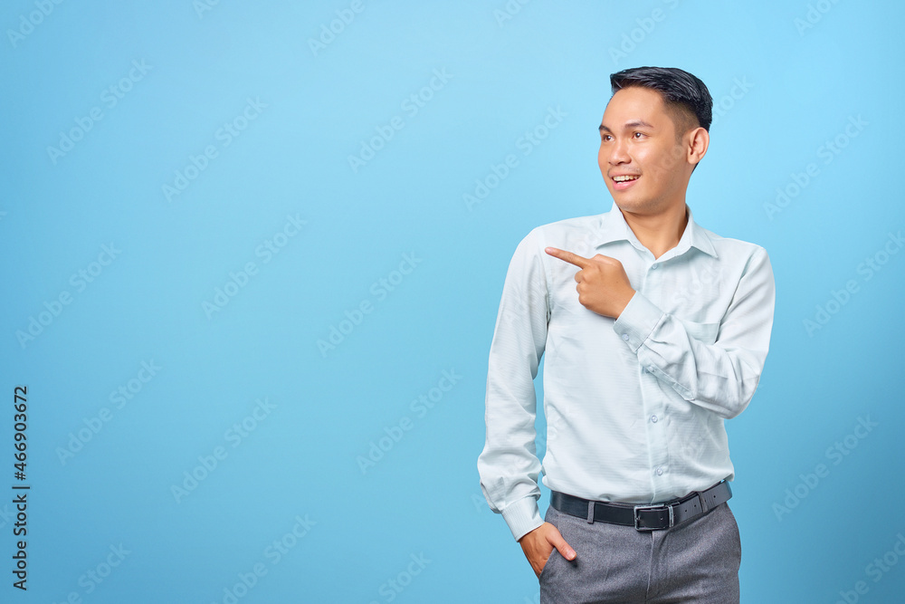 Smiling young handsome businessman pointing finger away at copy space on blue background Smiling young handsome businessman pointing finger away at copy space on blue background