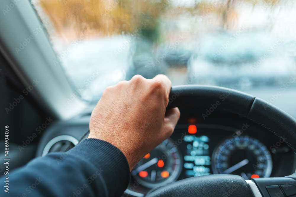 Driving a car in the rain, male hand grabbing steering wheel