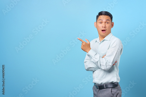 Shocked young handsome businessman pointing finger away at copy space on blue background