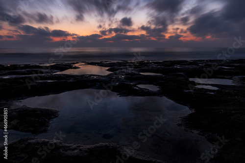 amazing scenic view at a sea shore from a coast after dramatic colorful sunset with flying blured clouds and reflection on water surface , beautiful ocean landscape