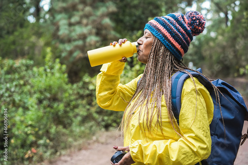 Senior african woman drinking water during trekking day into the woods - Travel concept - Focus on face