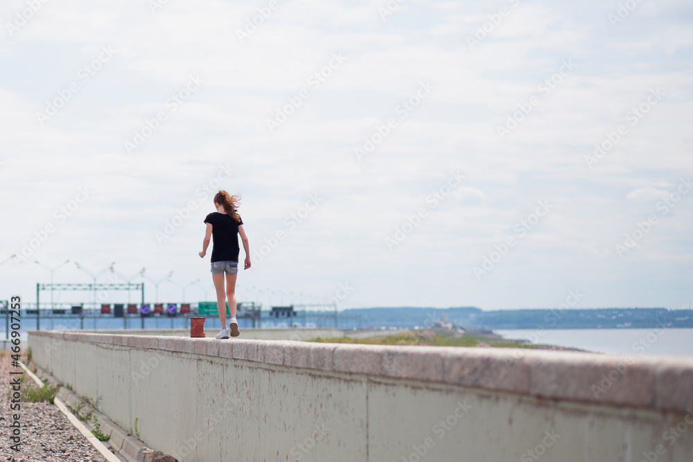 girl walks on the parapet between the bay and the road