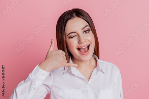 Photo of young cheerful lady show finger call me sign wink eye flirty isolated over pink color background