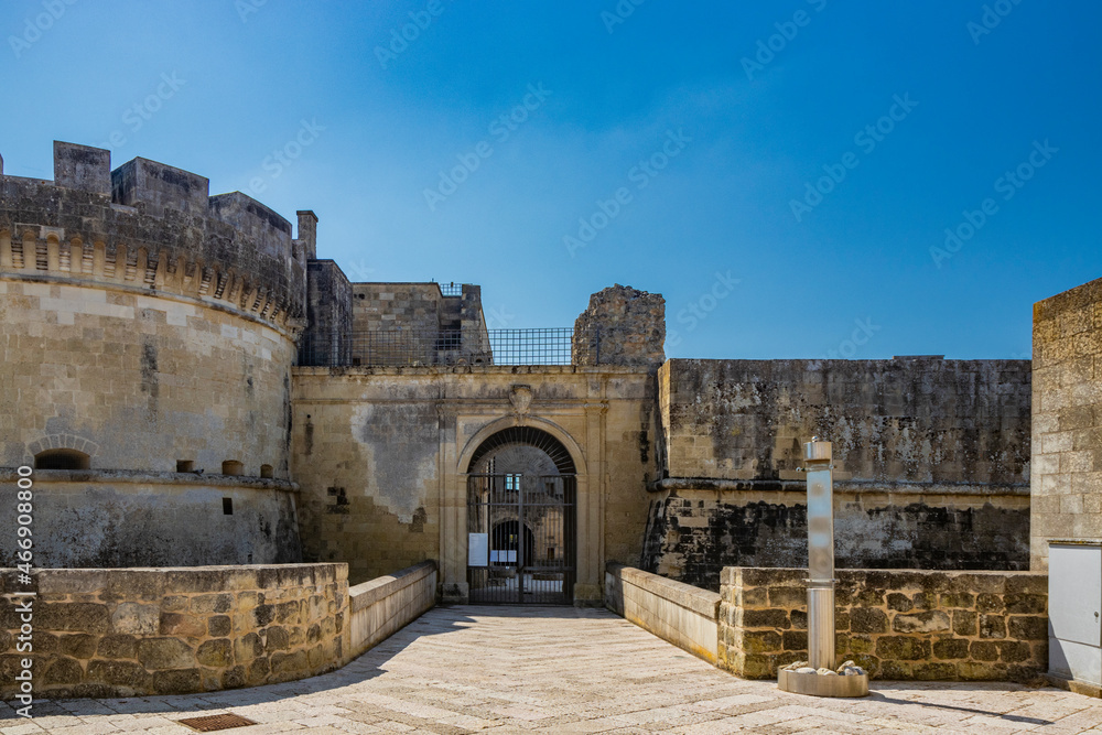 The small fortified village of Acaya, Lecce, Salento, Puglia, Italy. The large stone-paved square. The ancient medieval castle with towers and moat. The iron gate with the main entrance.