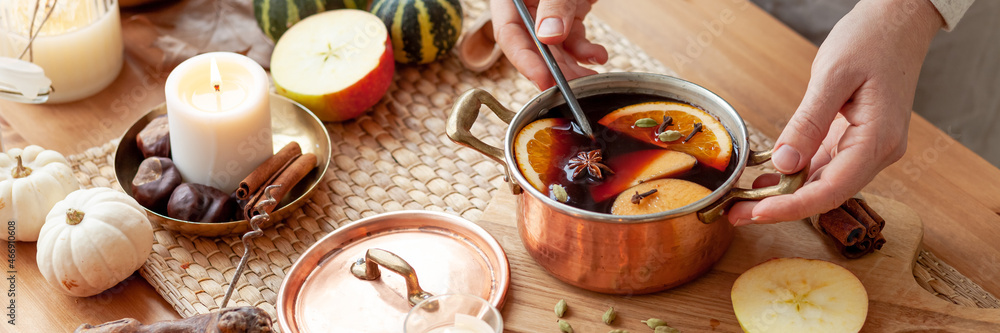 Young woman preparing hot autumn drink: mulled wine with spices, fruits. Natural ingreduents: cinnamon, anise, cardamon, clove, apple, orange. Cozy home atmosphere. Banner Young woman preparing hot autumn drink: mulled wine with spices, fruits. Natural ingreduents: cinnamon, anise, cardamon, clove, apple, orange. Cozy home atmosphere. Banner