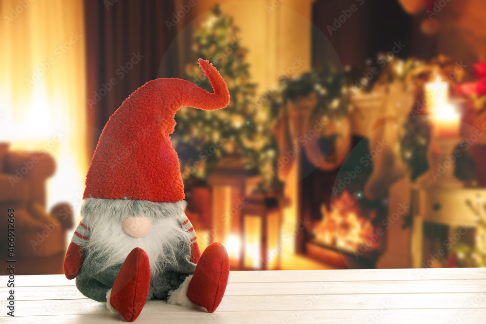 Fototapeta premium Funny Christmas gnome on white wooden table in room with festive decorations. Space for text