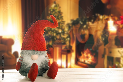 Funny Christmas gnome on white wooden table in room with festive decorations. Space for text