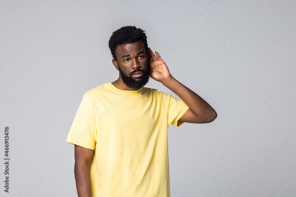 Say more loudly. Attractive happy afro-american man smiling and having his hand hear his ear and showing that he cant hear isolated on gray background Say more loudly. Attractive happy afro-american man smiling and having his hand hear his ear and showing that he cant hear isolated on gray background